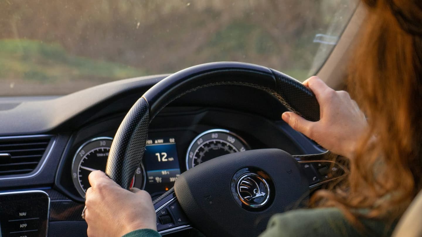 Jove conductora amb les mans al volant, llum natural de tarda — primera lliçó de conducció