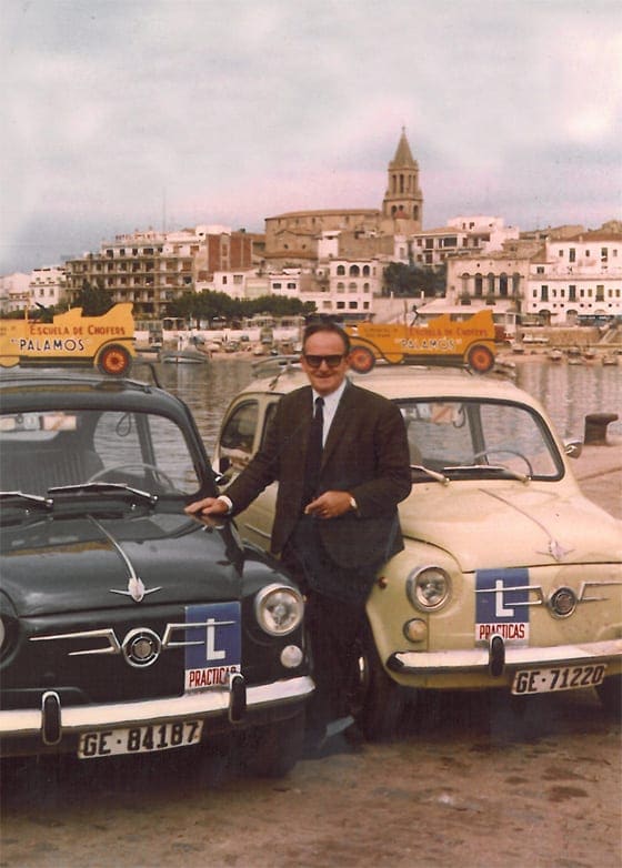 Lluís Puig Casanovas, fundador d'Autoescola Palamós, amb dos cotxes de pràctiques al port de Palamós